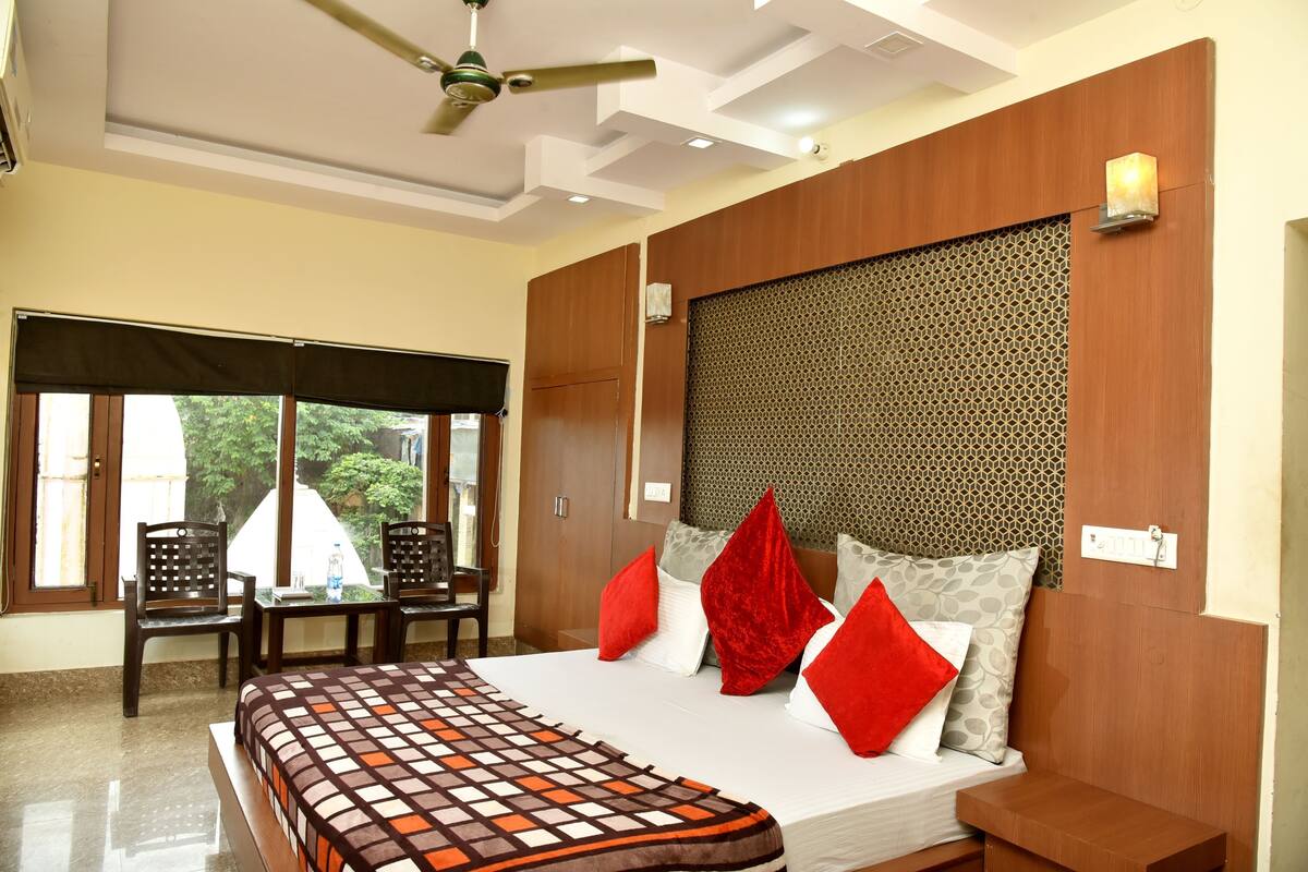 A hotel room with a bed, a ceiling fan, a window with a view, and a table with chairs.