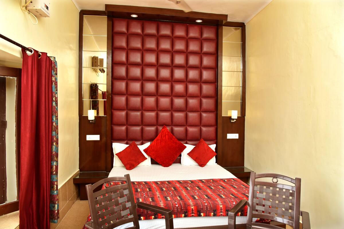 A hotel room with a large bed, red headboard, and two chairs.