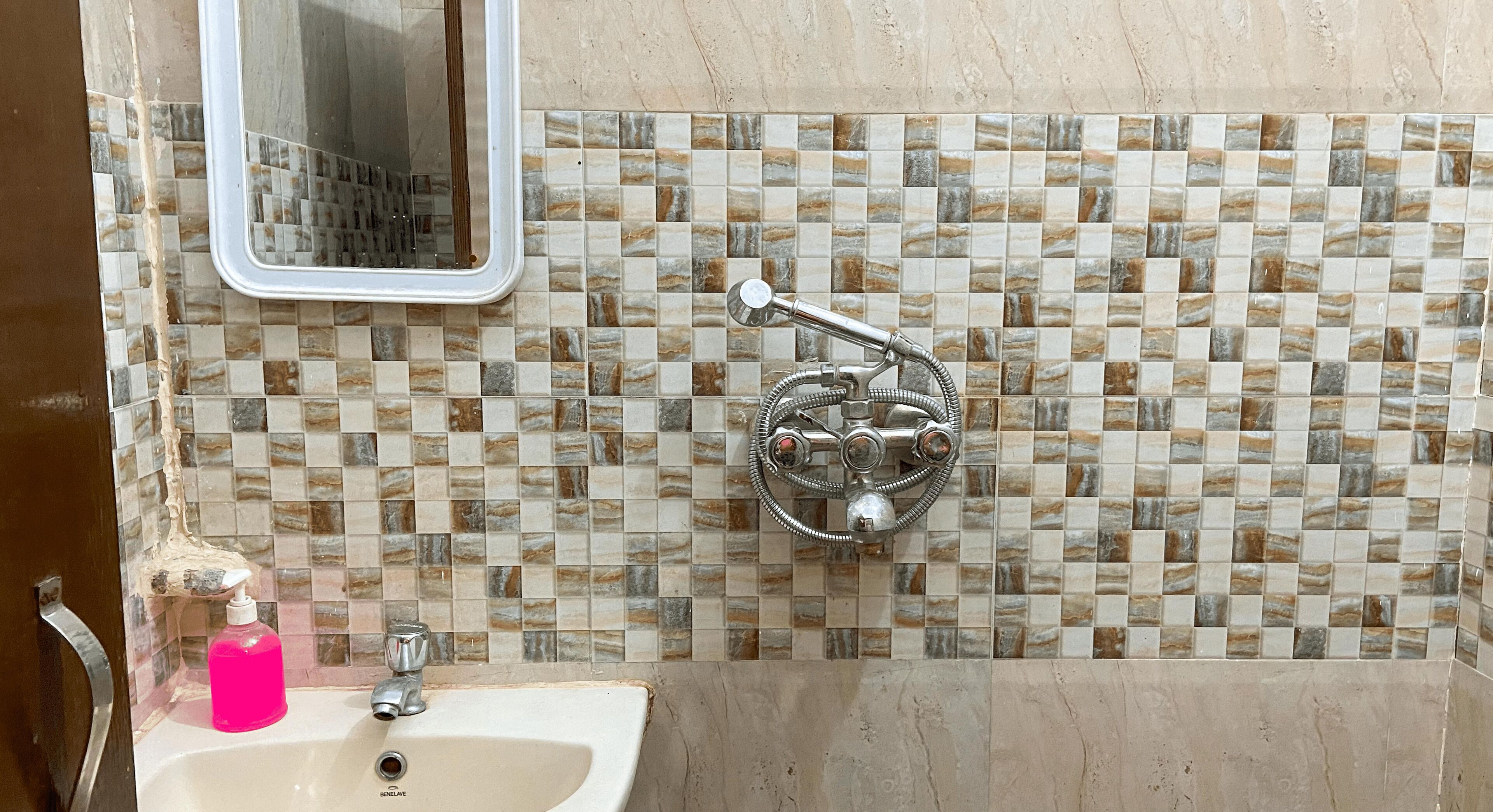 A bathroom with a sink, a mirror, and a shower with a mosaic tile wall.