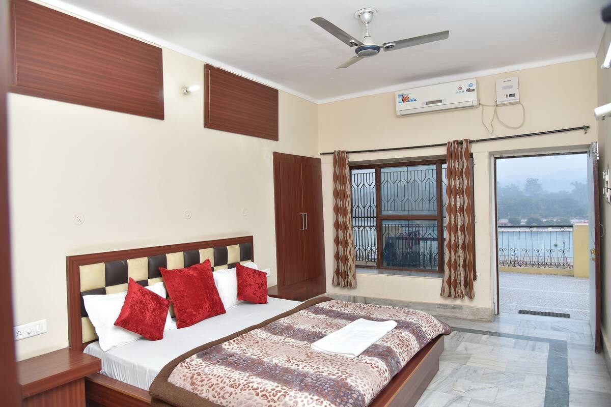 A bedroom with a bed, a ceiling fan, an air conditioning unit, a window with curtains, and a view of the outside.