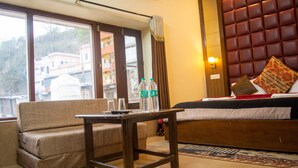 Habitación de hotel con sofá, una mesita, cama con cabecera y ventana con cortinas.