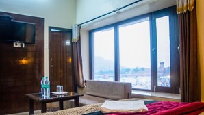 Habitación de hotel con una cama, una mesa con botellas de agua, una silla y un amplio ventanal con vistas a la ciudad.