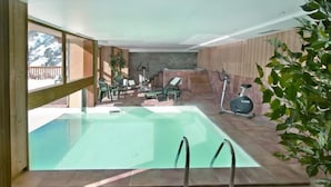 Una piscina interior amb vistes a les muntanyes, envoltada de parets de fusta i equipada amb cadires i una bicicleta d'exercici.