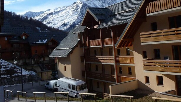 Una estació de muntanya amb edificis d'estil xalet, una zona d'aparcament i una muntanya coberta de neu al fons.