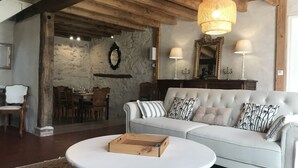 Una sala acogedora con un sofá blanco, una mesa de centro de madera y un comedor con una mesa y sillas de madera.
