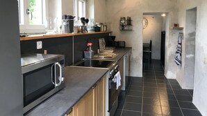 Una cocina moderna con horno empotrado, microondas y pileta. Hay una ventana que proporciona luz natural y una escalera que lleva a un nivel superior.