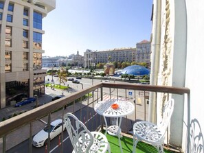 A balcony with white metal chairs and a small table, overlooking a city street with buildings and a blue dome structure. - Home-Hotel Kostelnaya 3 (Kyiv)