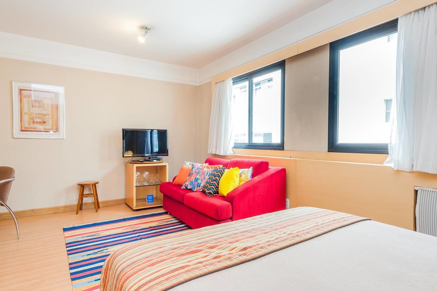 Une chambre d’hôtel avec un grand lit, un canapé rouge, un téléviseur posé sur un meuble en bois et une fenêtre avec des rideaux.