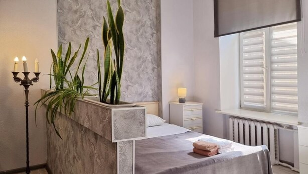 Un dormitorio moderno con cama, mesita de noche, lámpara y planta en maceta.