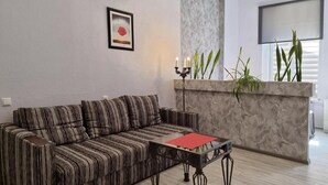 Una sala de estar con un sofá a rayas, una mesa de centro de vidrio, una chimenea y una planta.