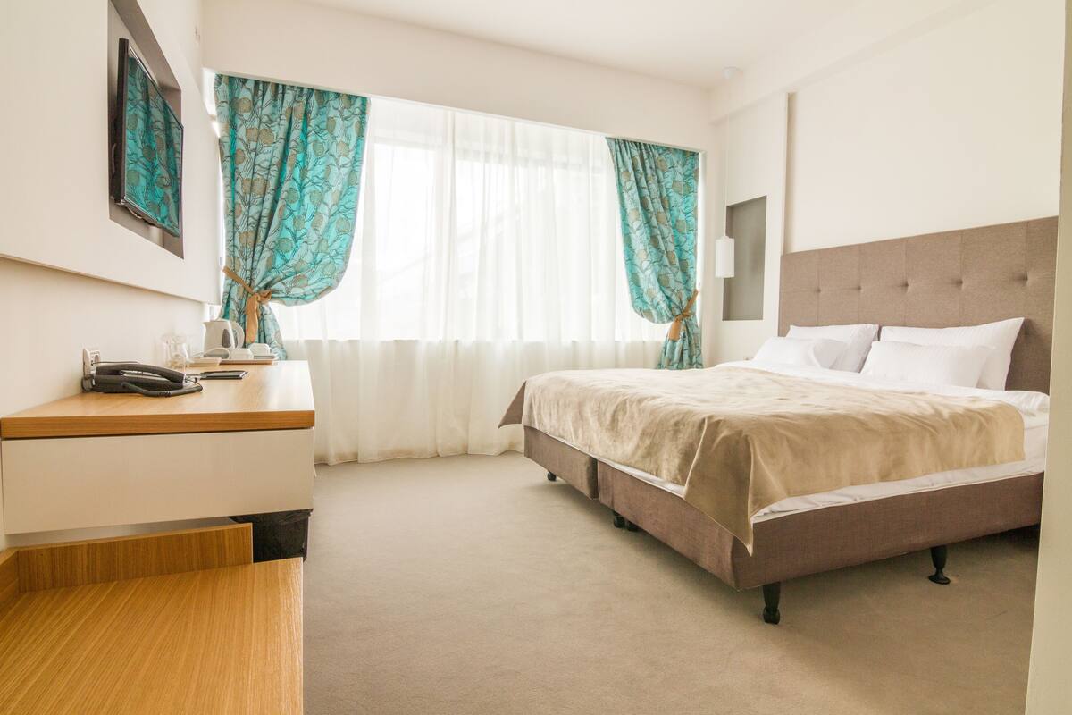 Una habitación de hotel con cama, escritorio y ventana con cortinas.