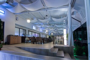 A spacious indoor area with a high ceiling, multiple tables and chairs, and a staircase leading to an upper level. - Gardenia Hotel & Spa (Veles)