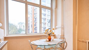 A dining area with a glass table and chairs, a vase with flowers, and a view of buildings through a large window. - Home-Hotel Khreschatyk 27 (Kyiv)