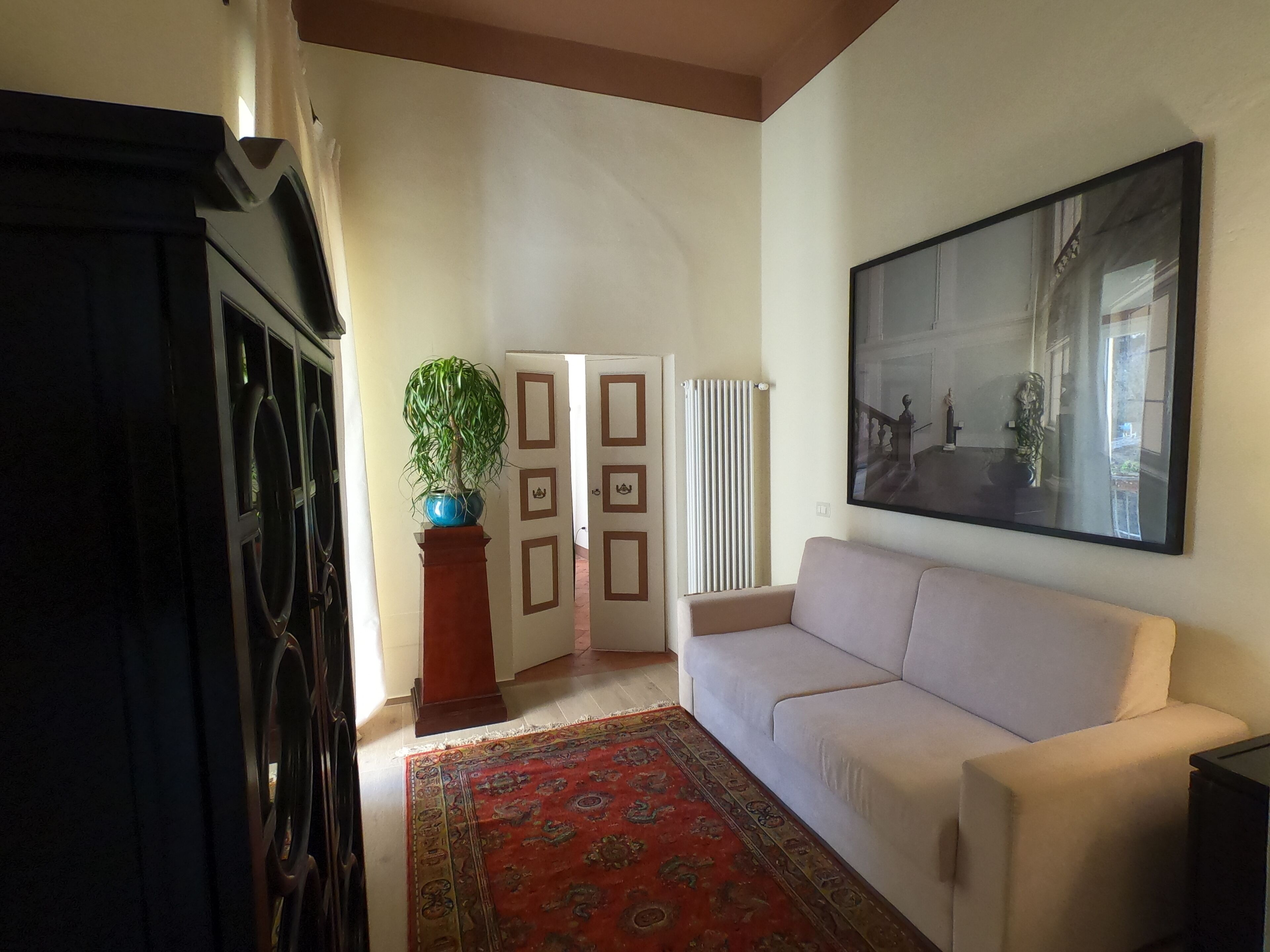 A living room with a white sofa, a red patterned rug, a blue vase with a plant, and a framed picture on the wall.