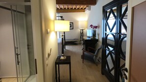 En gang med glasdør, skrivebord med lampe, stol og en potteplante.