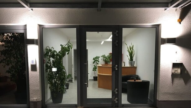 A building entrance with glass doors, potted plants, and a reception desk inside. - Main Kinzig Hotel am Limes (Erlensee)