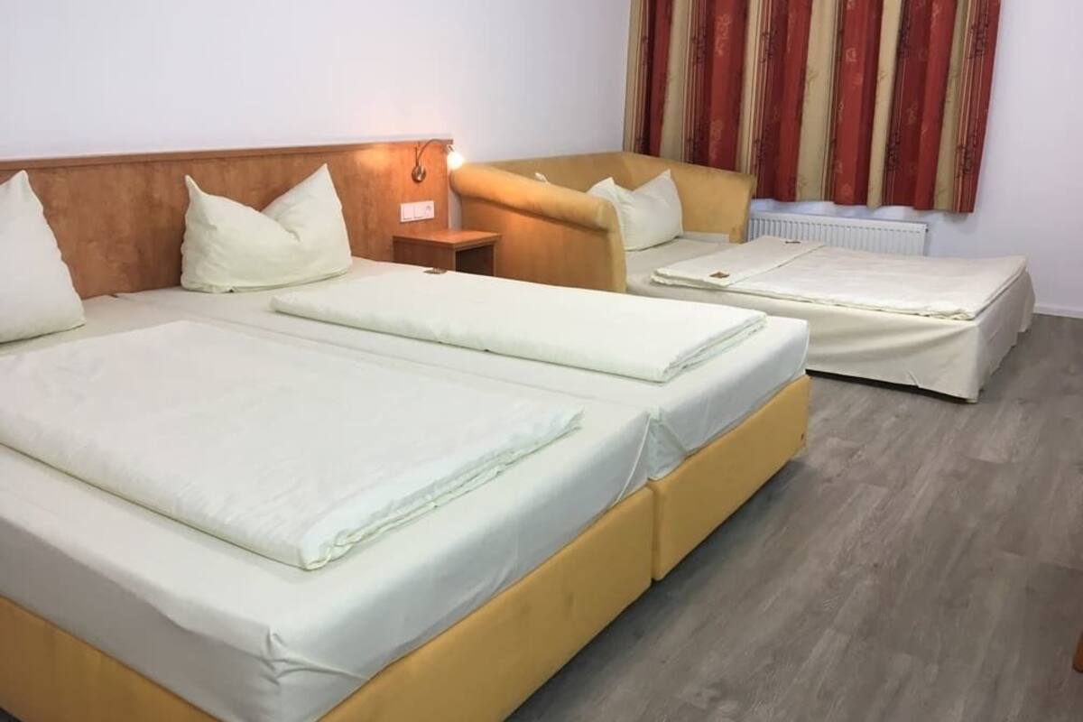 Ein Hotelzimmer mit zwei Betten, einem hölzernen Kopfteil, einem Nachttisch und einem Fenster mit Vorhängen.