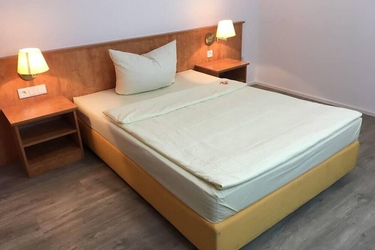 Ein Einzelbett mit Holz-Kopfteil, zwei Nachttische mit Lampen und eine kleine Ablagefläche.