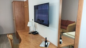 A hotel room with a wooden desk, a mounted TV, a mirror, a chair, and a bed with a striped pillow. - Main Kinzig Hotel am Limes (Erlensee)