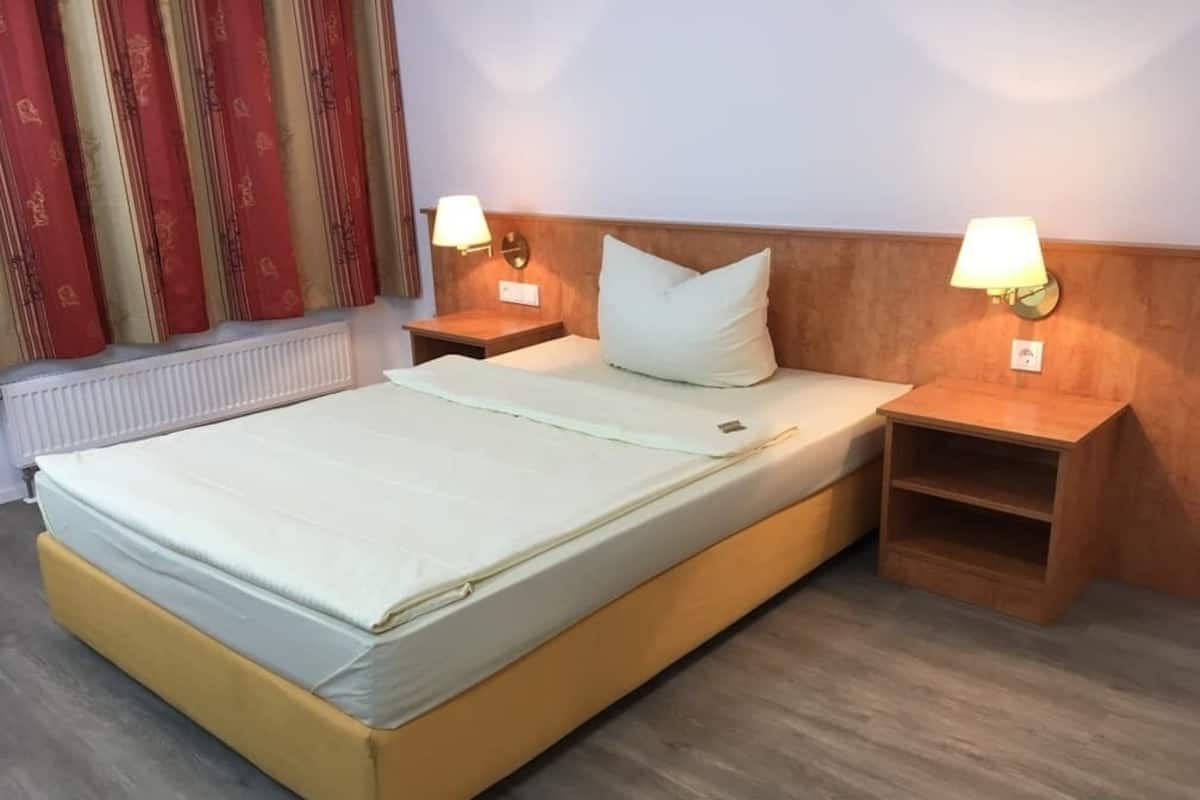 Ein Einzelbett mit hölzernem Kopfteil, zwei Nachttische mit Lampen und ein Heizkörper an der Wand.