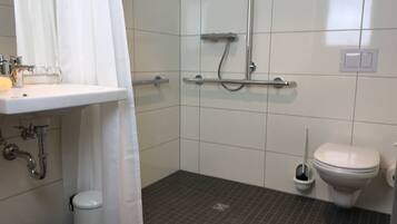 A bathroom with a white sink, a shower with a glass door, a toilet, and a trash bin.