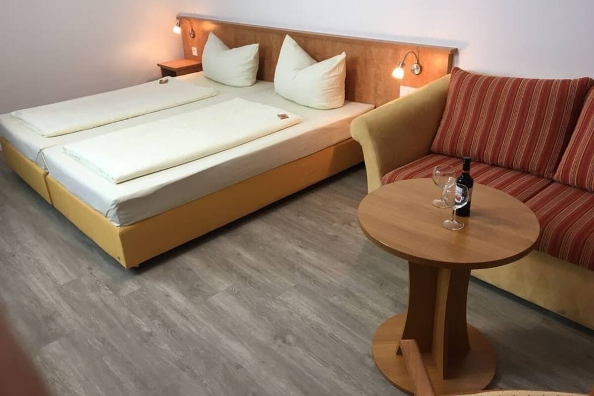 Ein Zimmer mit einem Bett, einer Schlafcouch und einem kleinen runden Tisch mit einer Flasche und einem Glas.