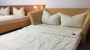 A bed with a wooden headboard, a beige sofa with pillows, and a bedside table with a lamp. - Main Kinzig Hotel am Limes (Erlensee)
