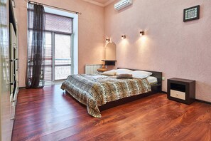 A bedroom with a large bed, a radiator, a nightstand, and a window with blinds.