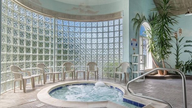 A hot tub area with a pool, chairs, and a view through a patterned glass wall.