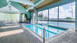An indoor swimming pool with stone flooring, large windows, and a view of the outside.