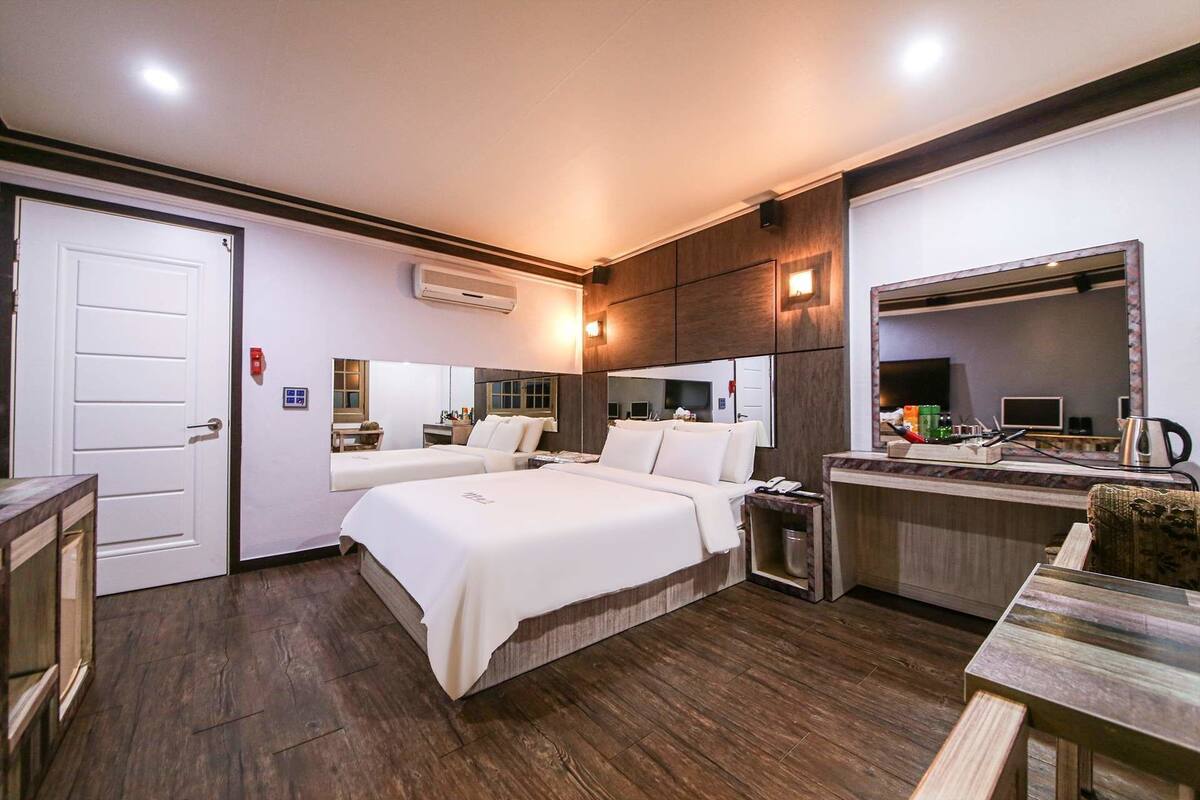 Una habitación de hotel con dos camas, un escritorio, un espejo y una kitchenette pequeña.