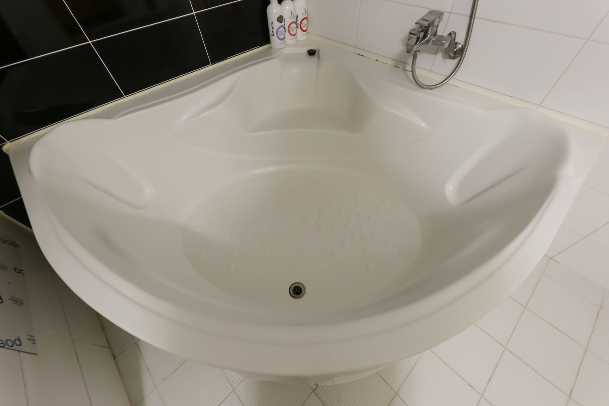 A white freestanding bathtub with a drain in a bathroom with white tiled walls and floor.