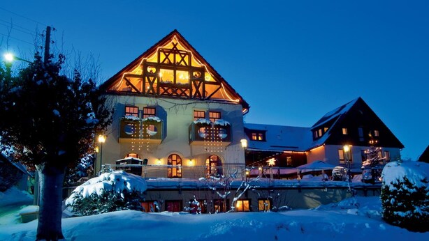 A large, multi-story building with a prominent gabled roof, illuminated windows, and snow-covered surroundings. - Hotel NEUE HÖHE (Klingenberg)