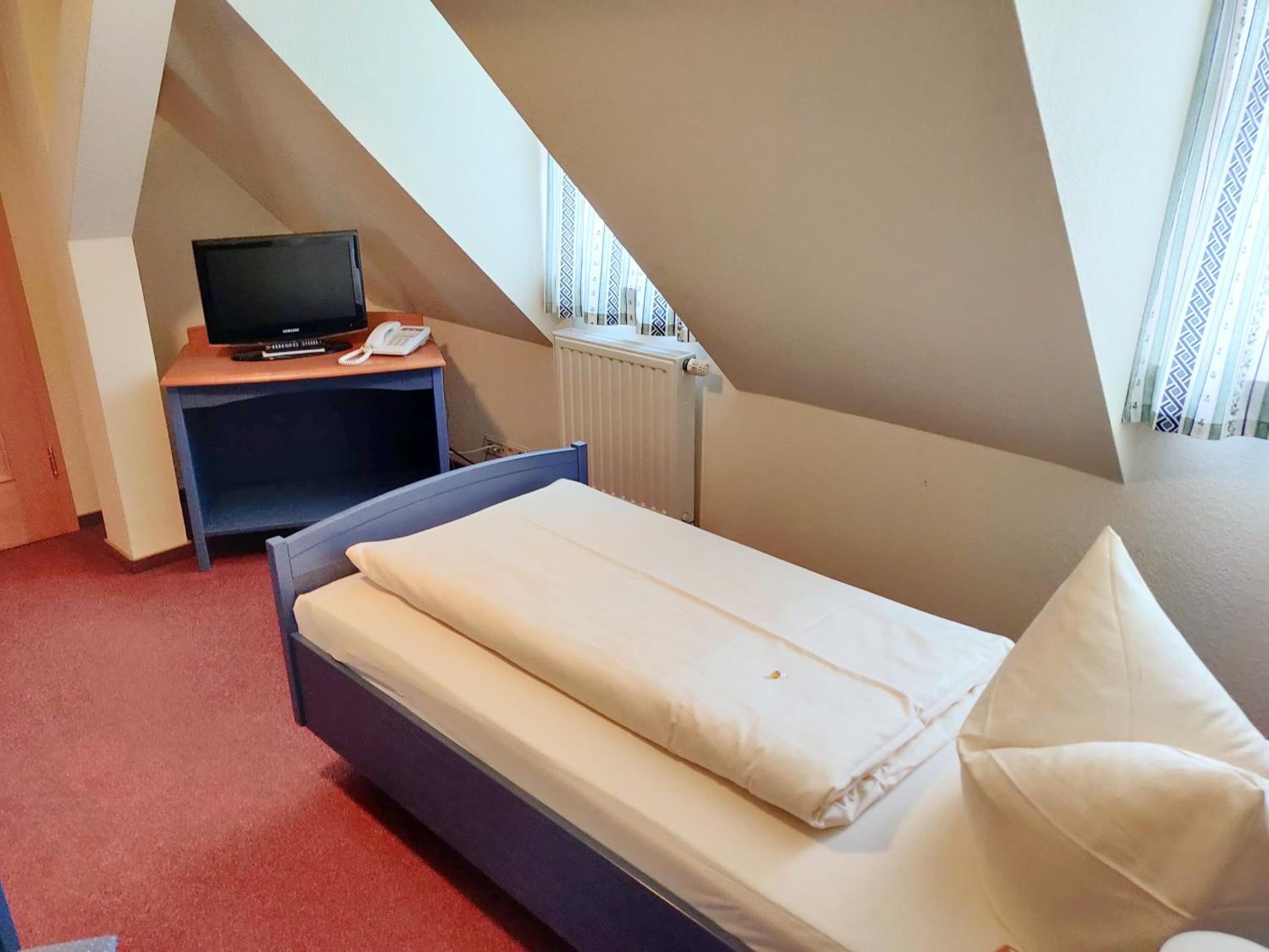 A small, single-bed room with a desk, a television, and a telephone.