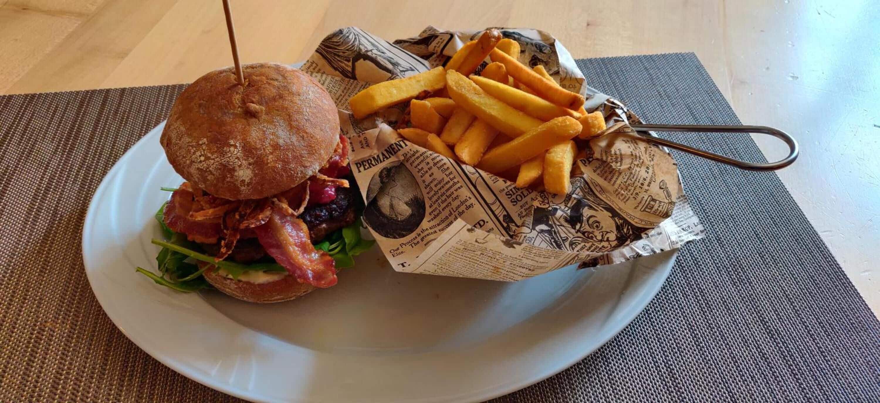 Un plato con una hamburguesa y papas fritas sobre un camino de mesa.