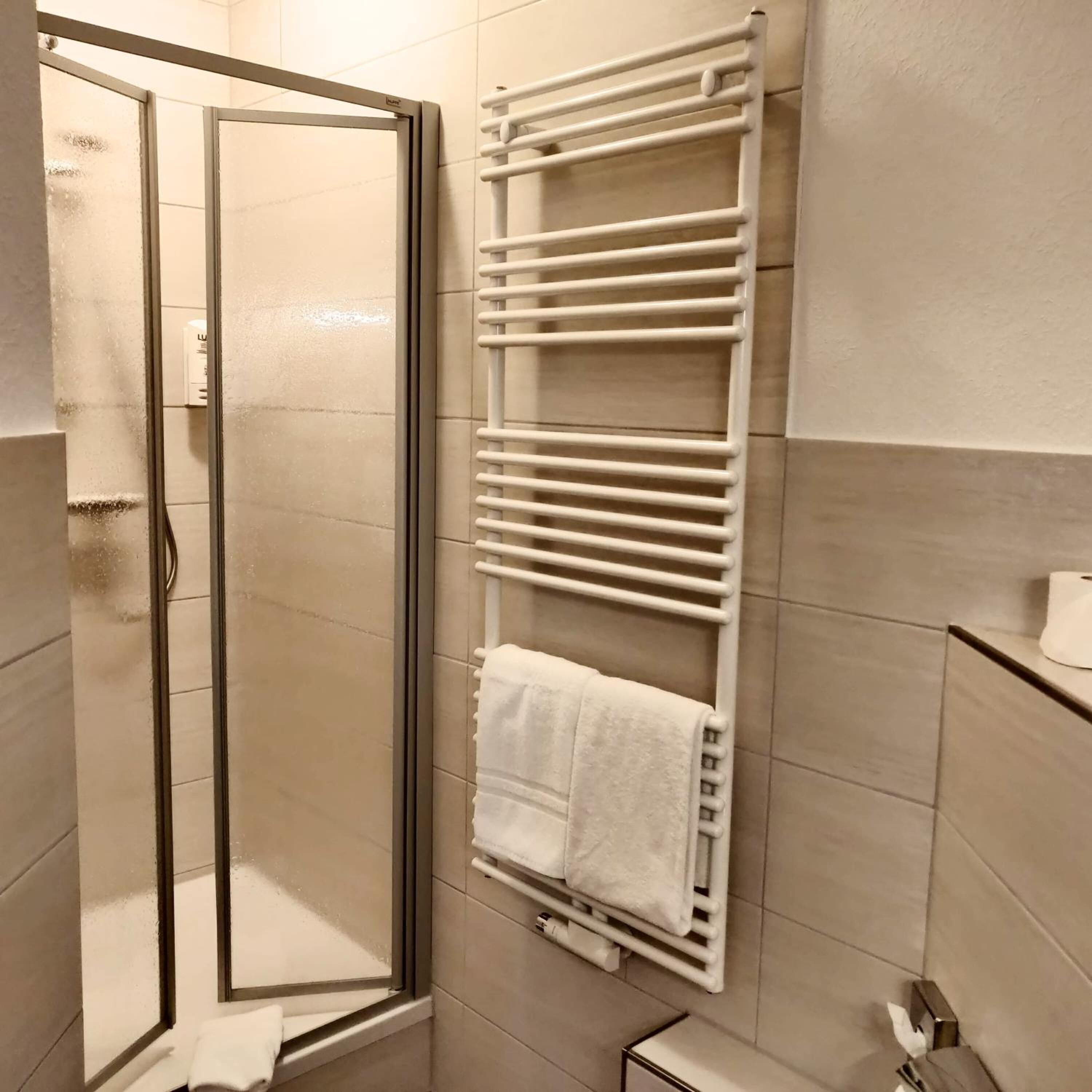 Un baño con cabina de ducha de vidrio, un toallero blanco con toallas y un inodoro.