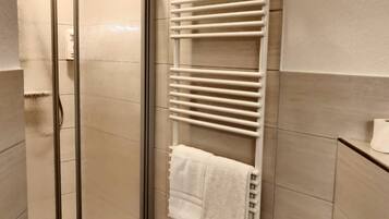Un baño con cabina de ducha de vidrio, un toallero blanco con toallas y un inodoro.
