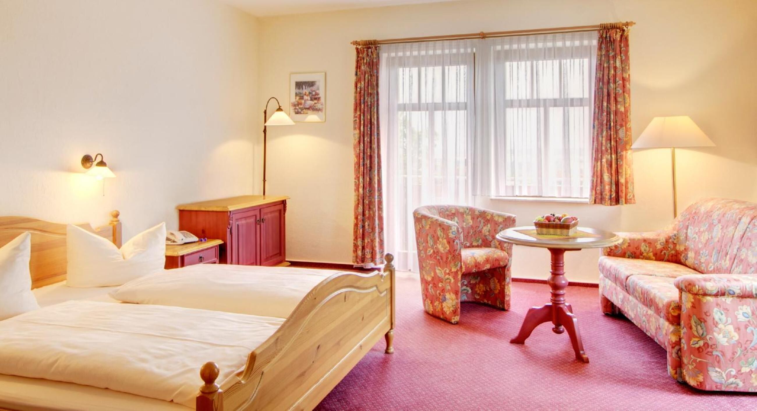 A hotel room with a bed, a desk, a chair, a sofa, and a table with a fruit basket.