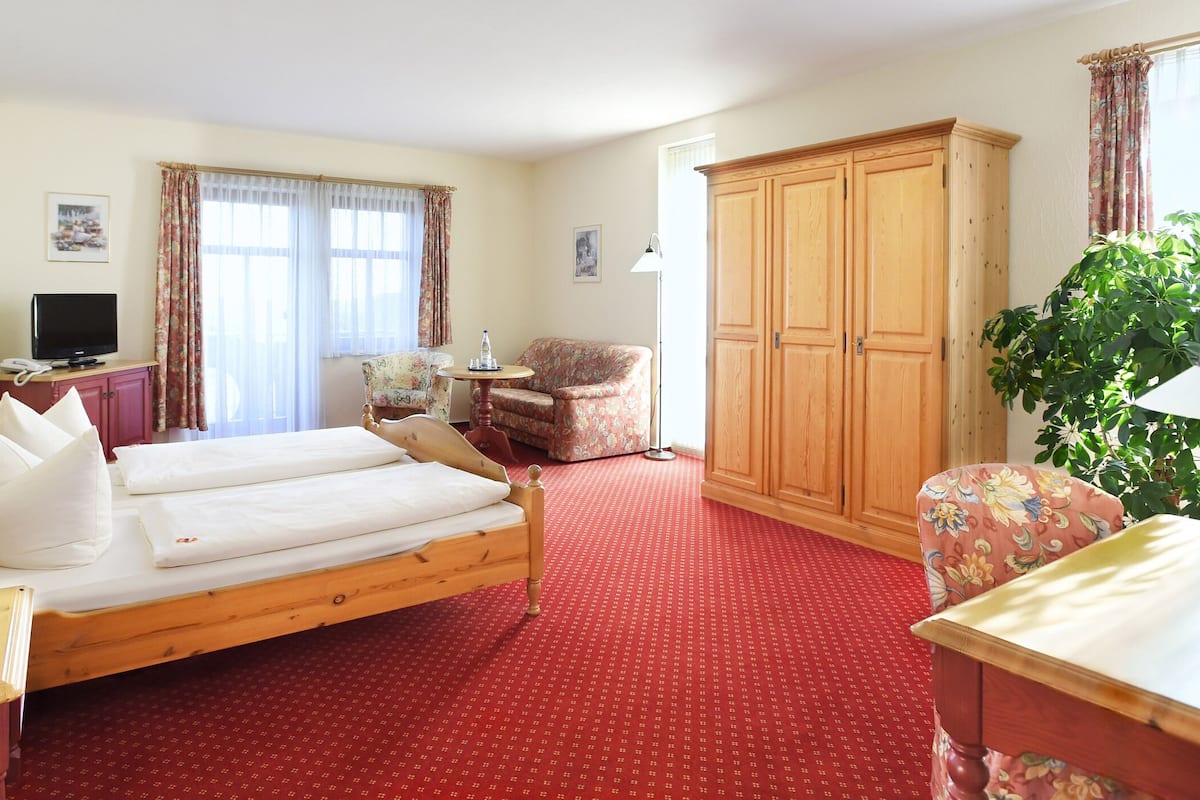 Quarto de hotel com cama, escrivaninha, cadeira, guarda-roupa e uma planta.