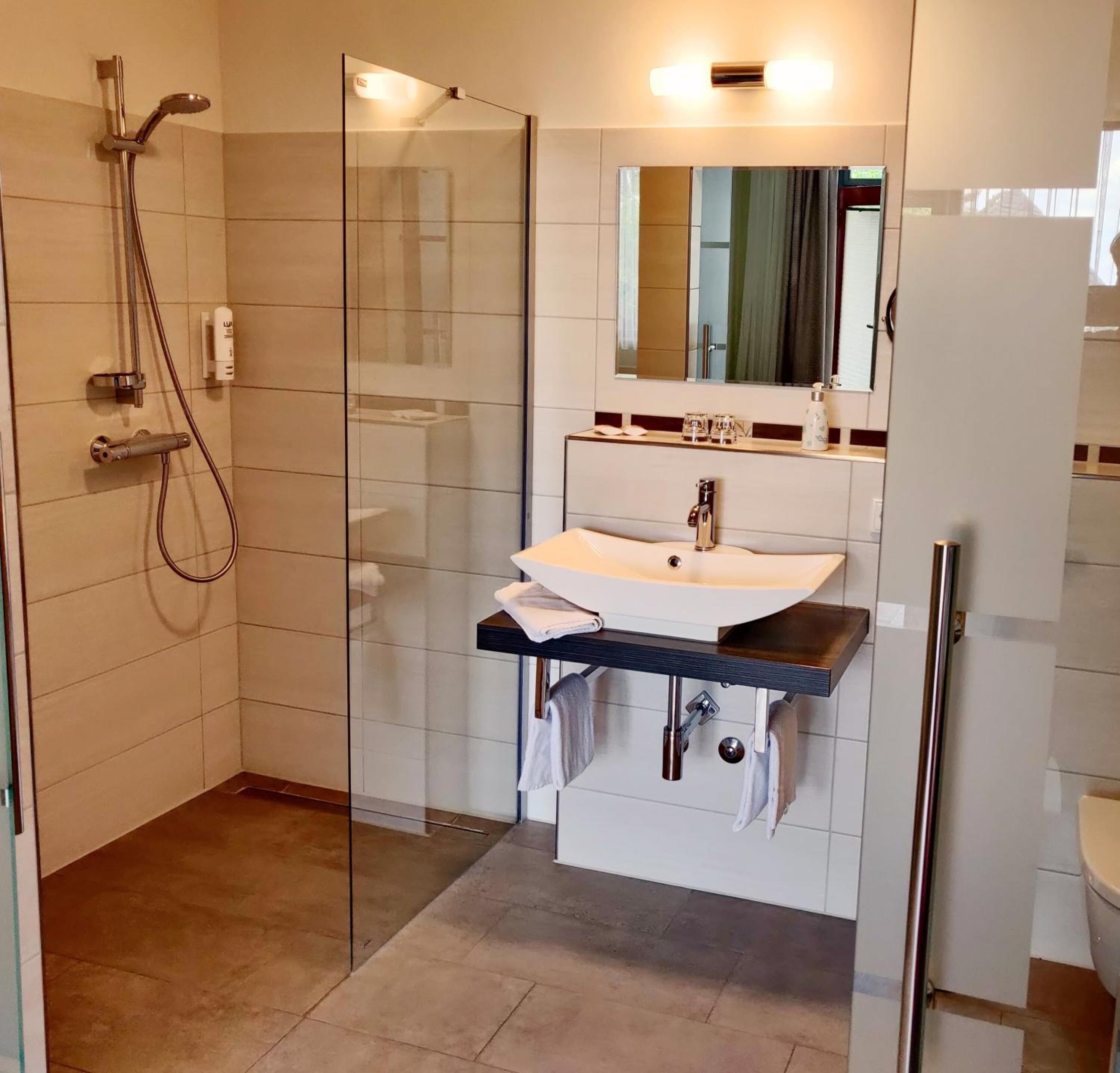 A modern bathroom with a glass-enclosed shower, a white sink with a dark countertop, and a mirror above the sink.
