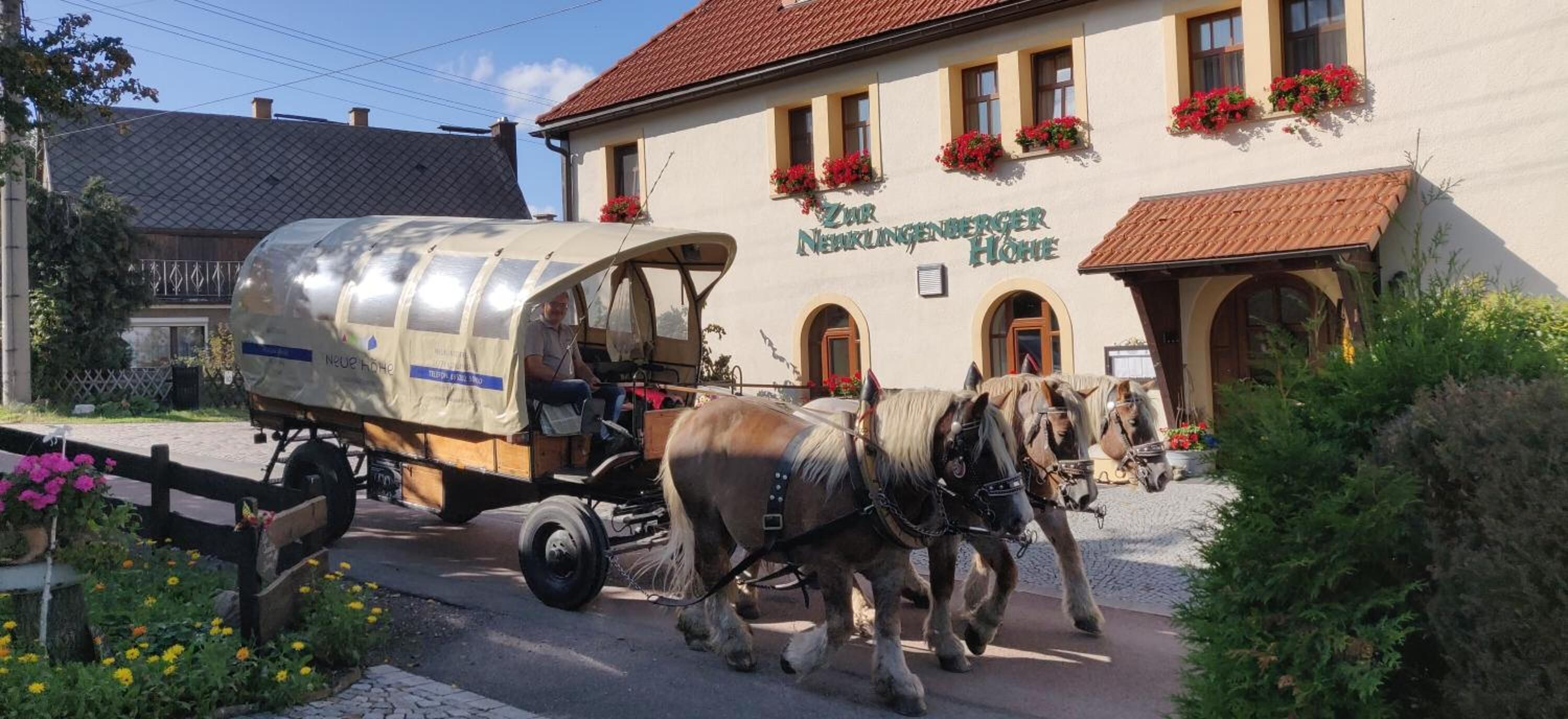 Eine traditionelle Kutsche vor einem Gebäude mit der Aufschrift "Zur Neunkunftner Hohhe".