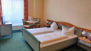 Habitación de hotel con cama doble, escritorio con computadora, silla y mesita con lámpara.