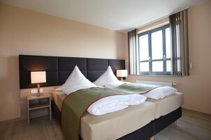 A hotel room with a large bed, two bedside tables, a window with curtains, and a headboard.