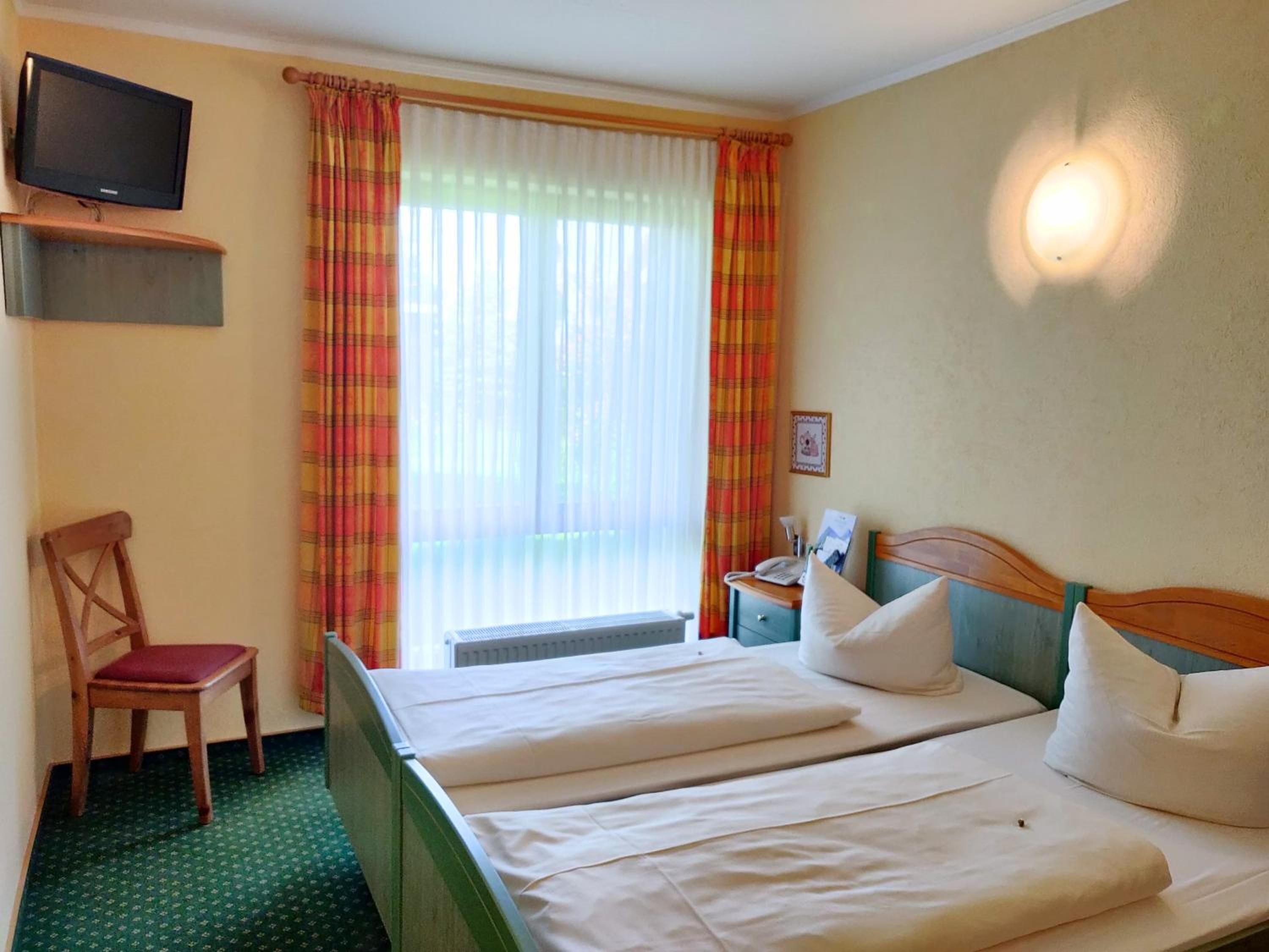 Une chambre d’hôtel avec deux lits, un téléviseur fixé au mur, une chaise et une fenêtre avec des rideaux.