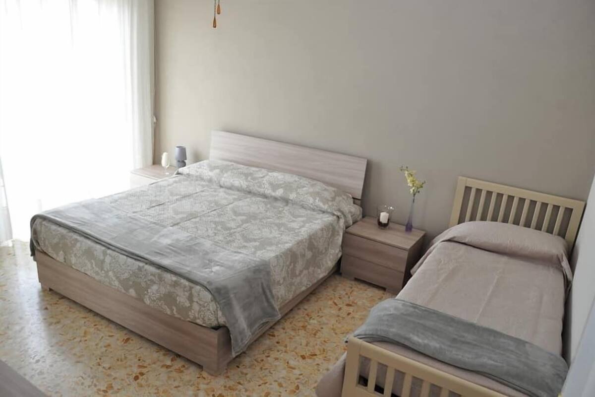 A bedroom with a large bed, bedside tables, a nightstand, and a vase with flowers.