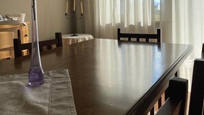 A dining area with a wooden table, chairs, a vase with flowers, and sheer curtains. - Sweet Emma (Caserta)