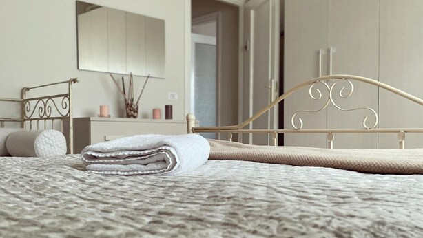 A neatly made bed with a textured blanket, a metal headboard, and a bedside table with a candle and decorative items. - Sweet Emma (Caserta)