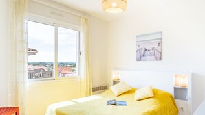 Ein Schlafzimmer mit einem großen Bett, einem Fenster mit Vorhängen, einem Nachttisch mit Lampe und Blick auf Gebäude.