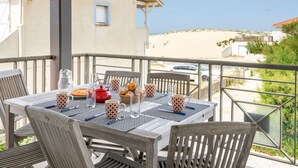 Ein Tisch für zwei auf einem Balkon mit Blick auf das Meer und ein Gebäude im Hintergrund.