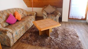 A cozy living room with a wooden ceiling, a patterned sofa, a chair, a small wooden table, and a fluffy rug. - Schwarzwaldblick by Interhome (Schonach)